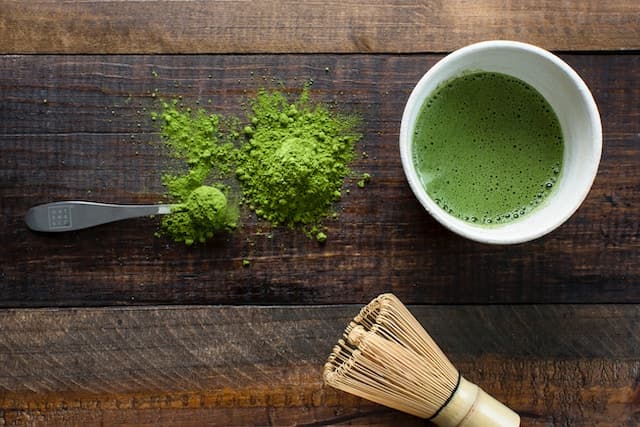 Green tea in white ceramic mug beside brown wooden brush